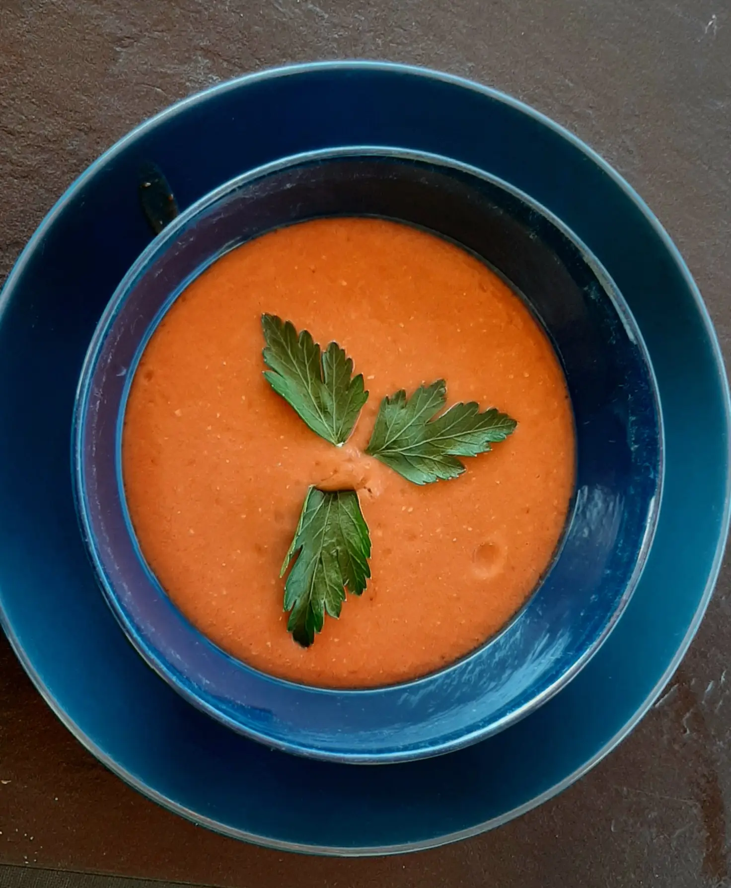 Eine tiefe blaue Schale mit kalter Gazpacho, mit drei Petersilienblättern angerichtet.