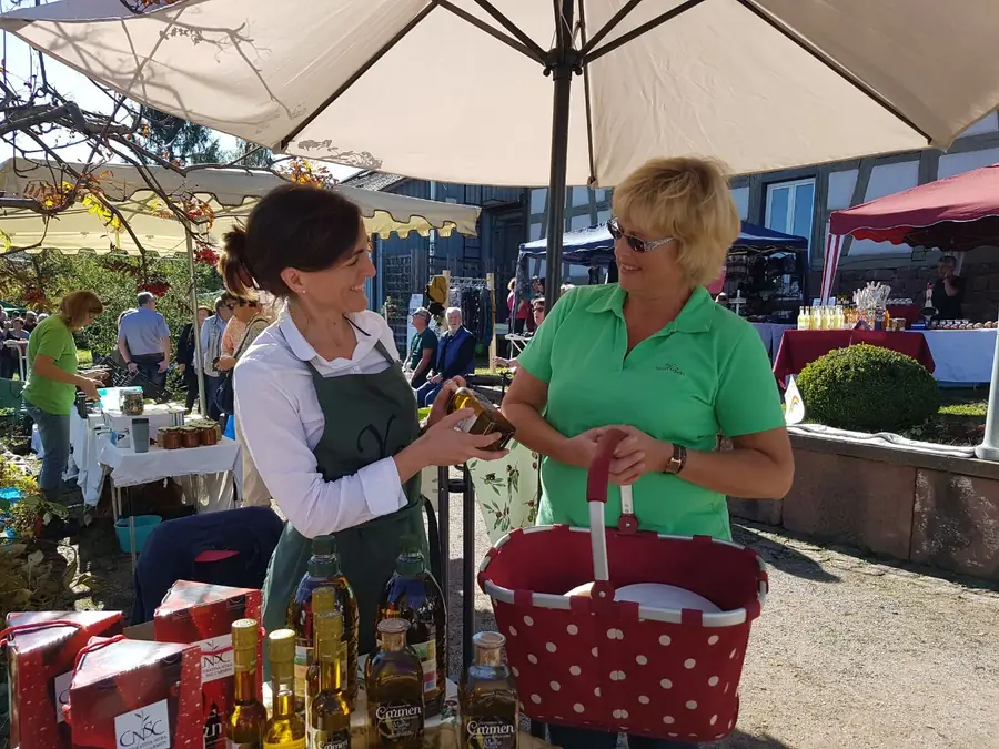 Yolanda Cabrera reicht einer Kundin am Marktstand eine Flasche Olivenöl.